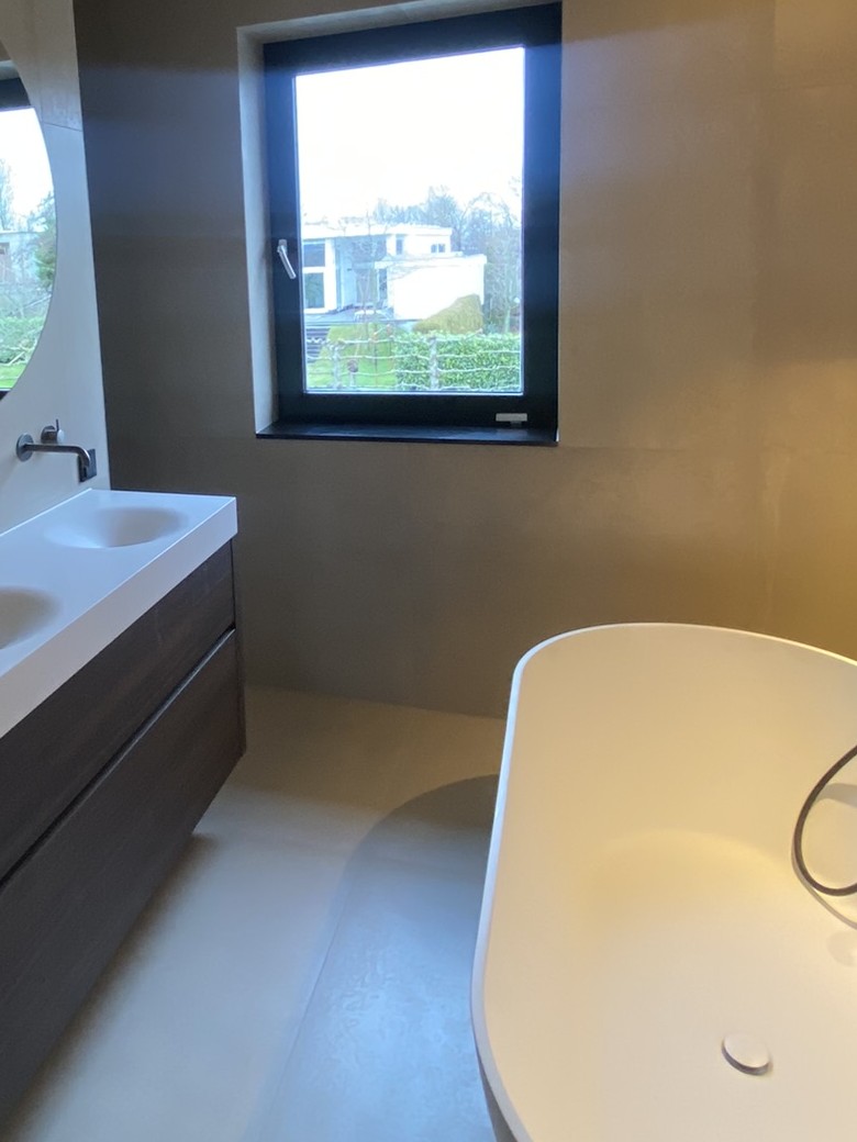 Badkamer met vrijstaand bad, dubbele wastafel op een donker houtlook meubel en een raam